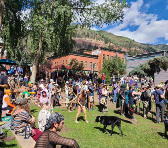 Camp Alderwild festivalgoers in Elks Park with the New Sheridan Hotel and Telluride mountains behind