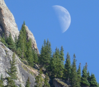 Moon above a rocky cliff and evergreen trees in Bear Creek near Telluride, Colorado