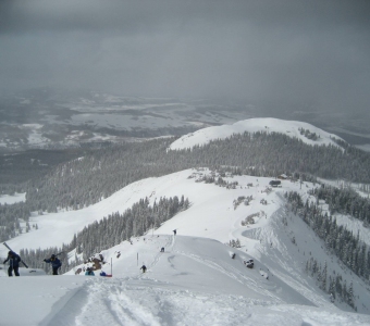 Skiers ascending a snowy ridge above Prospect Bowl at Telluride Ski Resort, with Bald Mountain in the distance.