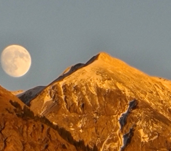 Moon rising between mountain peaks above Ophir, Colorado, in evening light